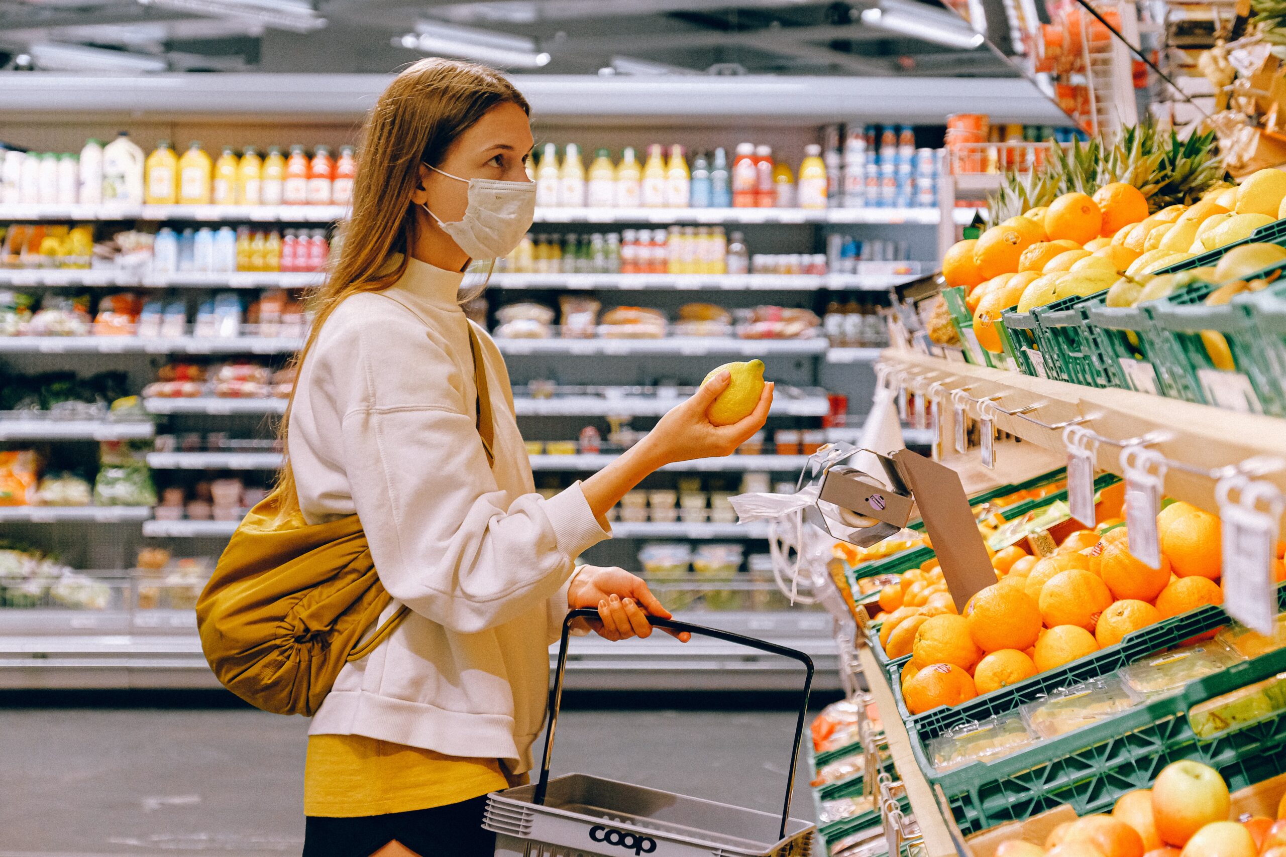 Woman in Yellow Tshirt and Beige jacket Holding a Fruit From the FruitStand